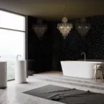 Luxurious bathroom with a large window, freestanding tub, twin pedestal sinks, black mosaic walls, and chandeliers.