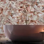 Luxurious bathroom with a large round white tub against an earthy textured wall, a lit candle, and a bottle of wine.