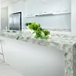 Modern kitchen featuring a green and white mosaic island countertop, white cabinets, and stainless steel appliances.