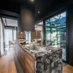 Modern kitchen with a sleek stone and wood island, large windows, bright natural lighting, and a spiral staircase.