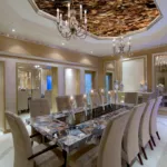 Luxurious dining room featuring a large marble table, plush chairs, elegant chandeliers, and a vibrant blue aquarium.