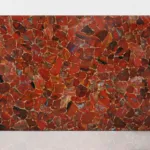 Vibrant red stone slab with a mosaic of irregular shapes and a glossy, textured surface reflecting light.