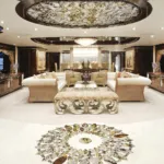 Luxurious yacht interior with elegant sofas, an intricate ceiling, detailed floor patterns, and warm lighting.