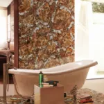 Luxurious bathroom with a clawfoot tub, brown and beige marble walls and floor, and a small table with books.